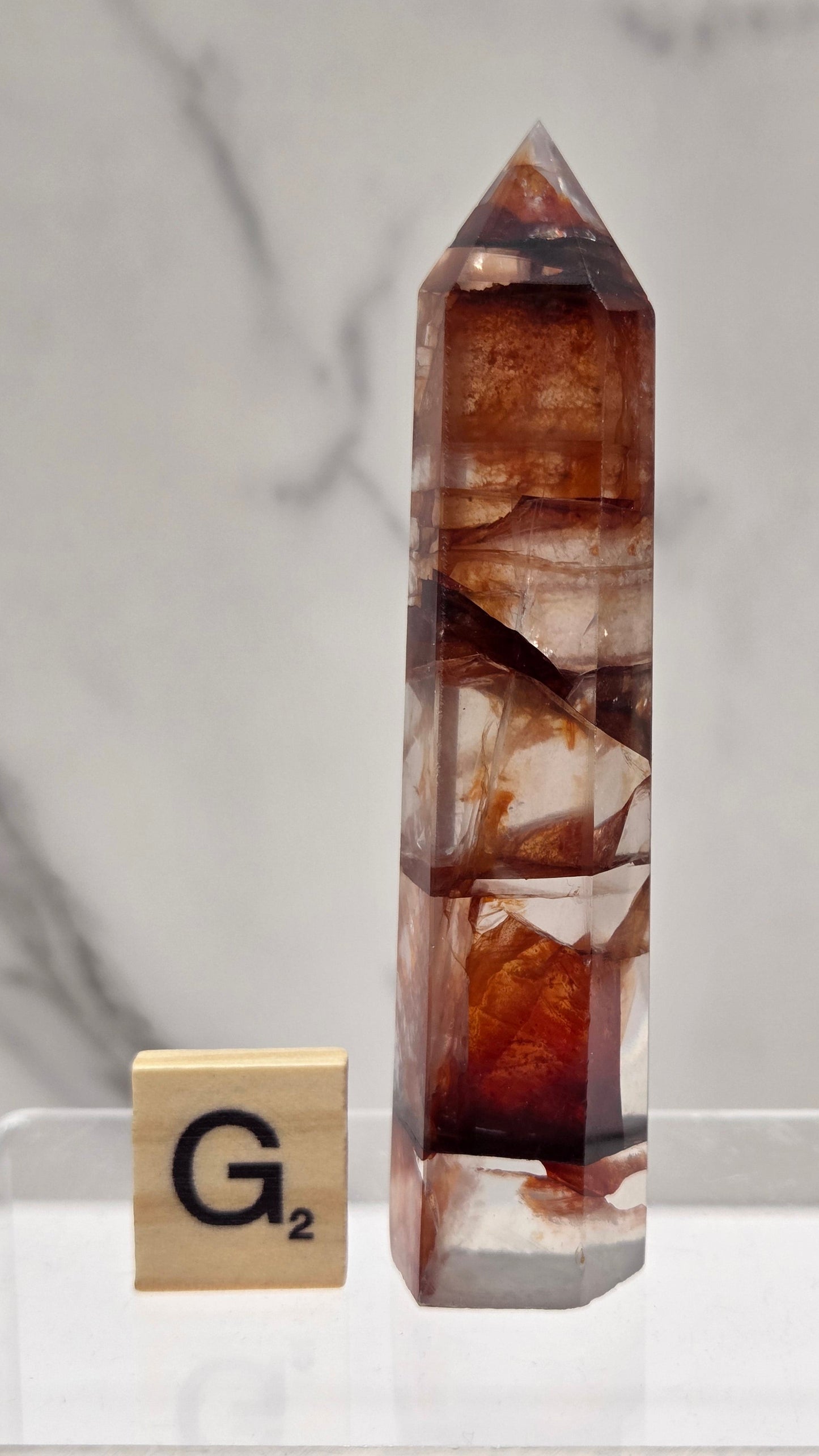 fire quartz crystal point on a white stand against a marble background