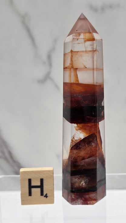 fire quartz crystal point on a white stand against a marble background
