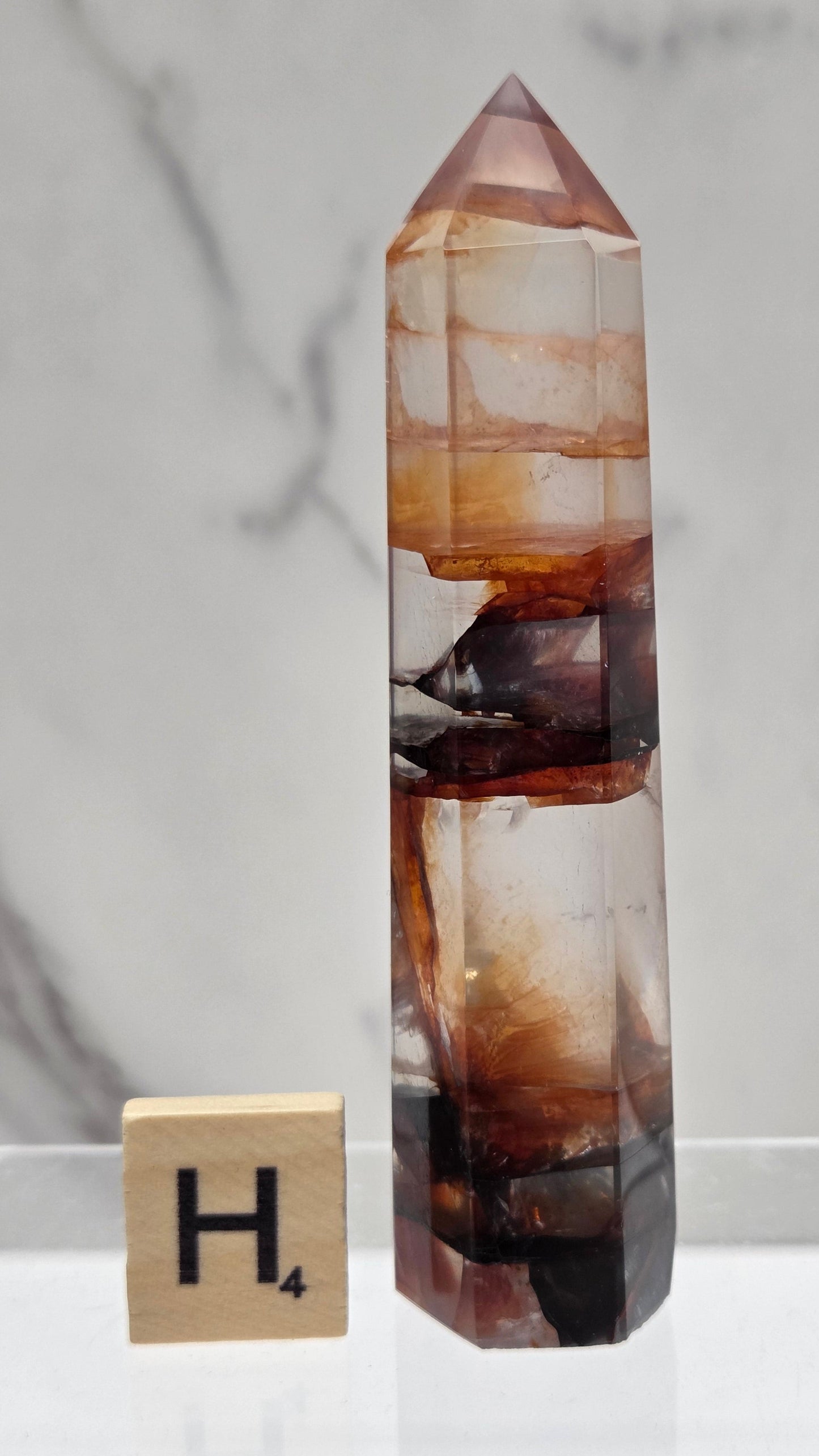 fire quartz crystal point on a white stand against a marble background