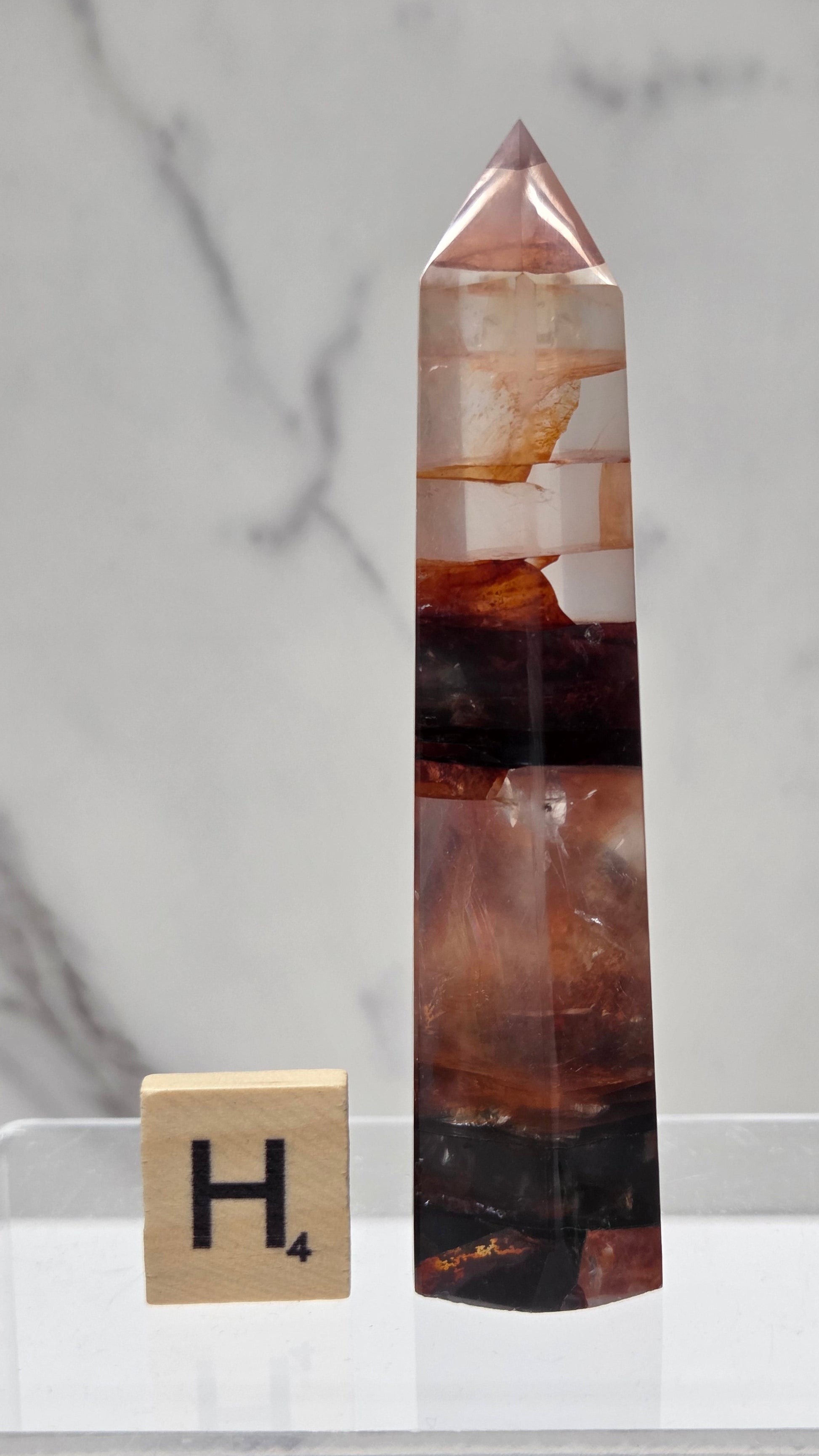 fire quartz crystal point on a white stand against a marble background