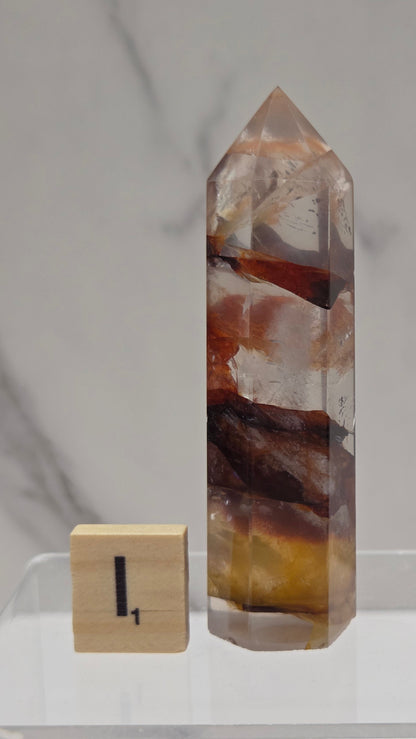 fire quartz crystal point on a white stand against a marble background