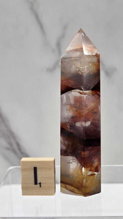 fire quartz crystal point on a white stand against a marble background