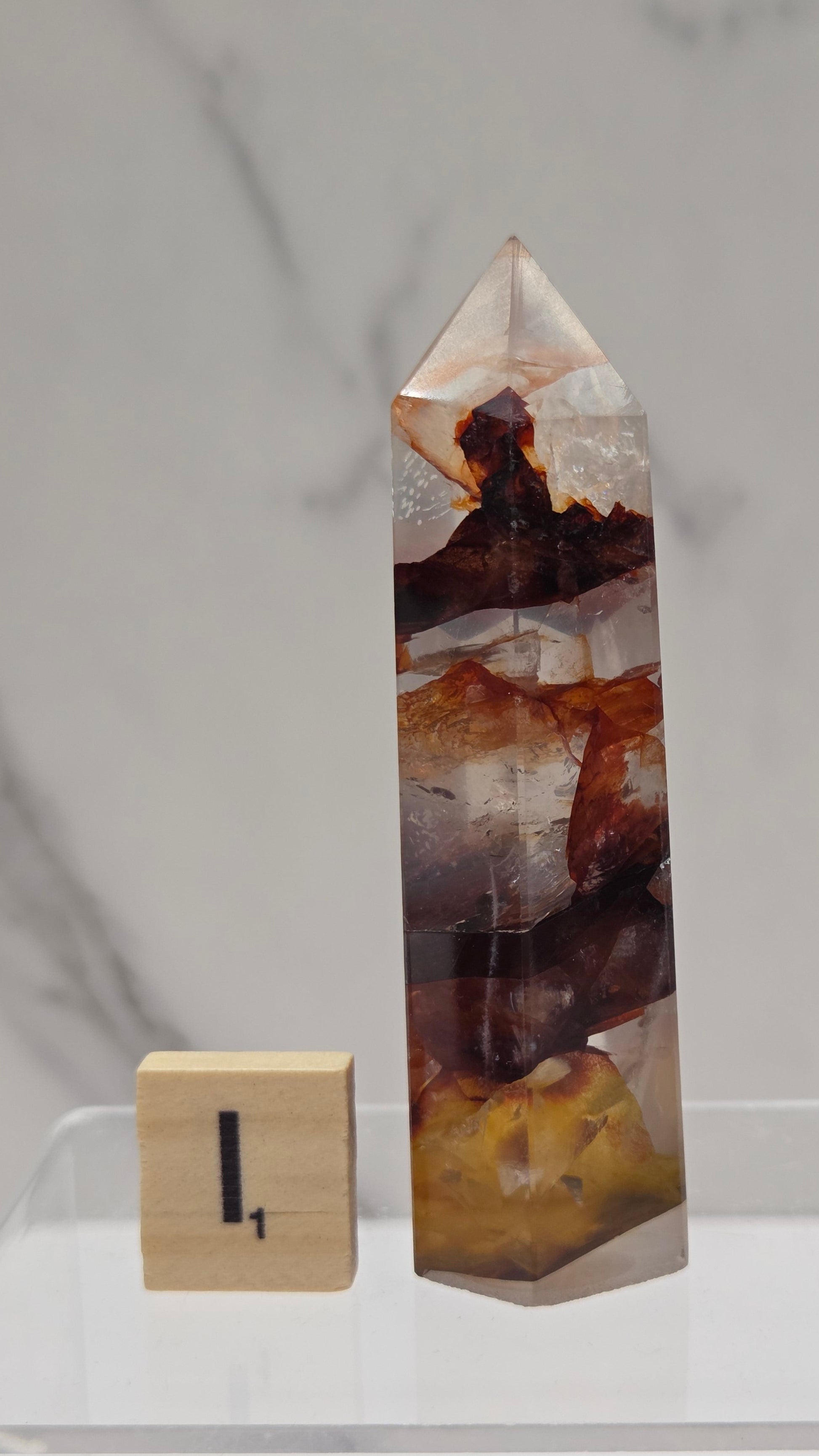 fire quartz crystal point on a white stand against a marble background