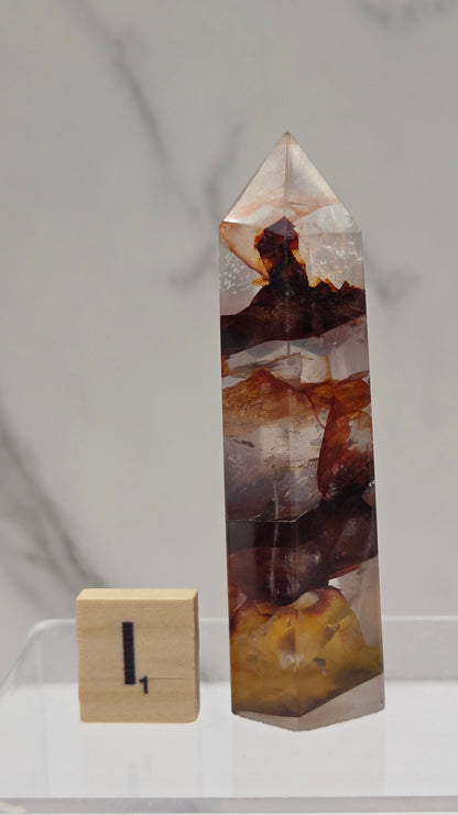 fire quartz crystal point on a white stand against a marble background