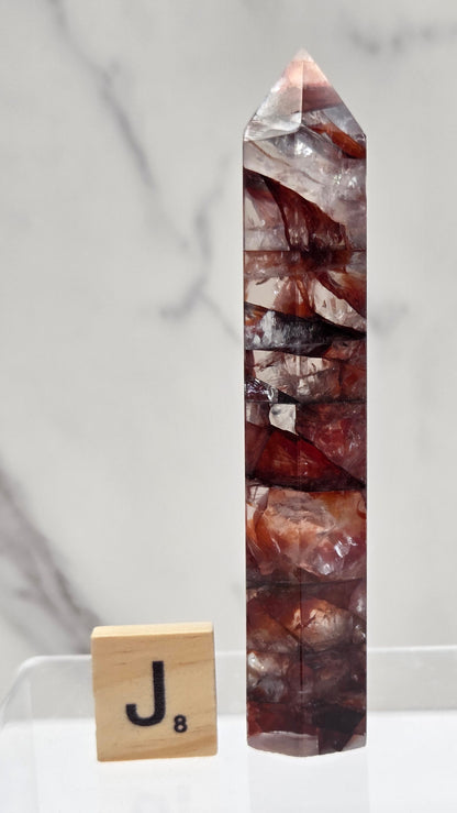 fire quartz crystal point on a white stand against a marble background