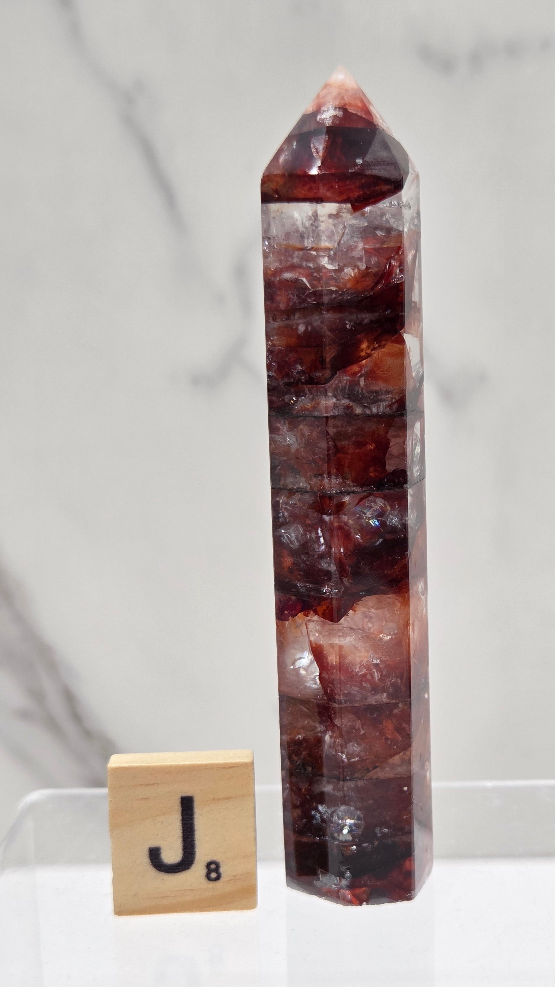 fire quartz crystal point on a white stand against a marble background