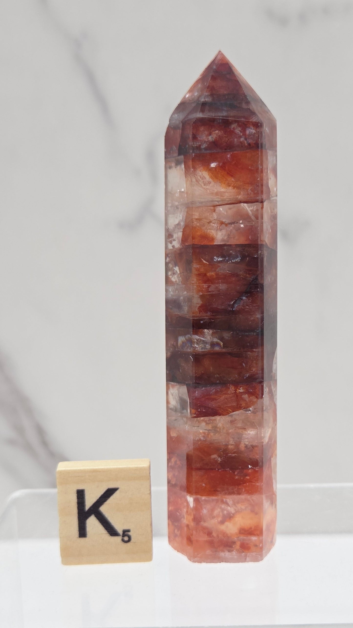 fire quartz crystal point on a white stand against a marble background