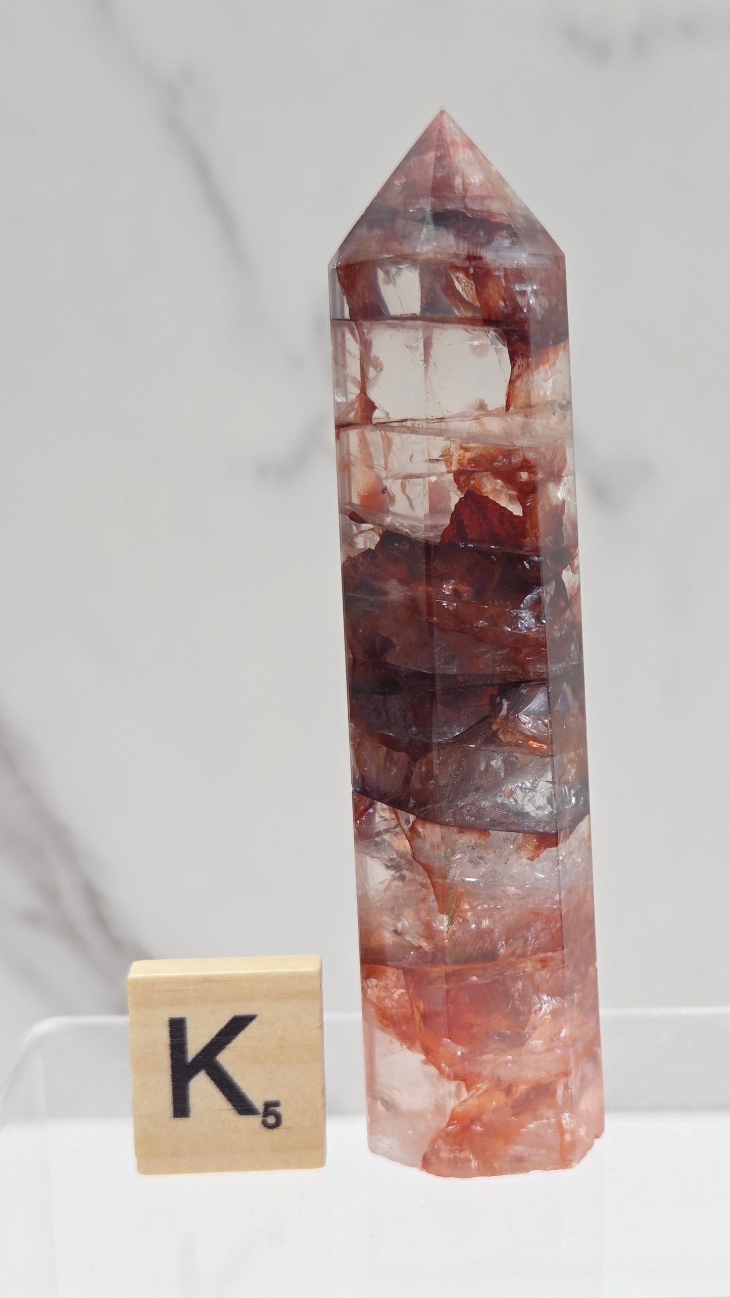 fire quartz crystal point on a white stand against a marble background