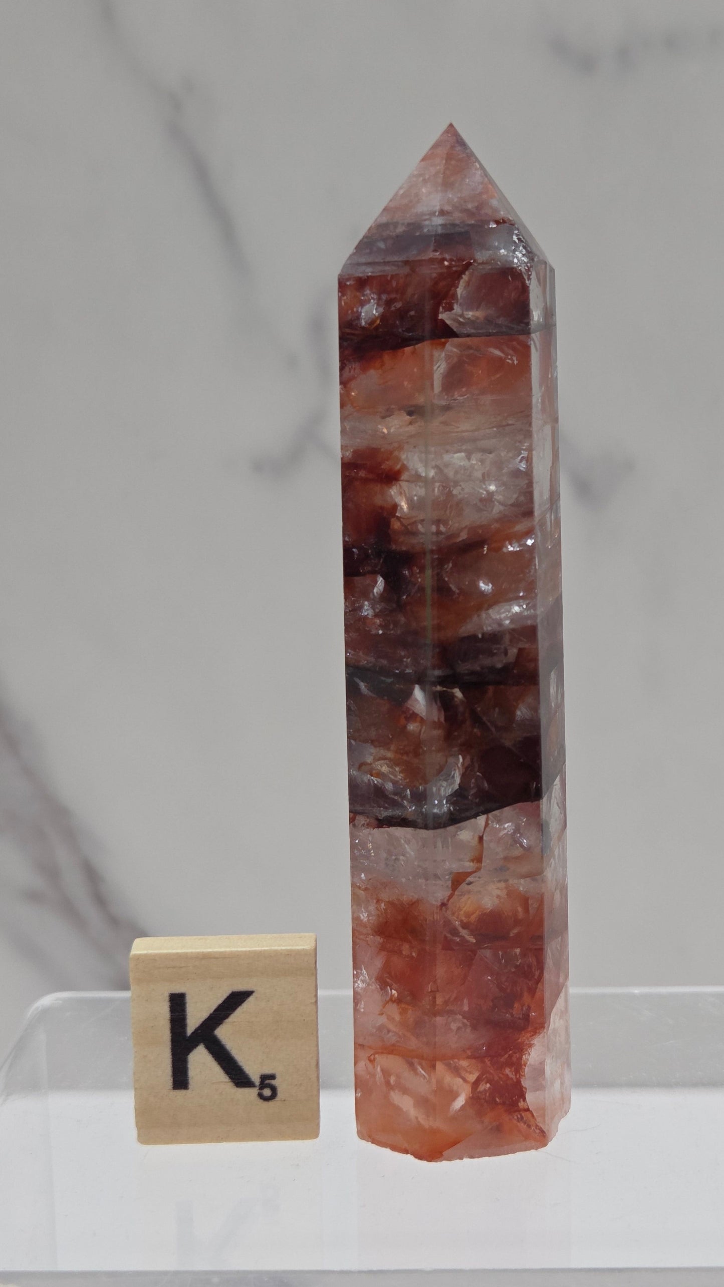 fire quartz crystal point on a white stand against a marble background