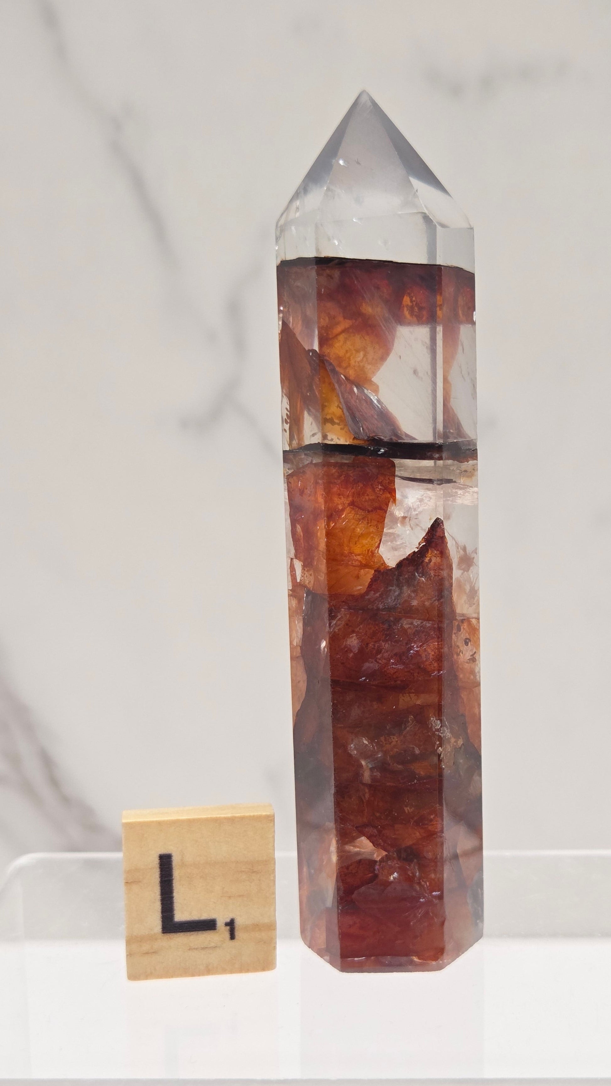 fire quartz crystal point on a white stand against a marble background
