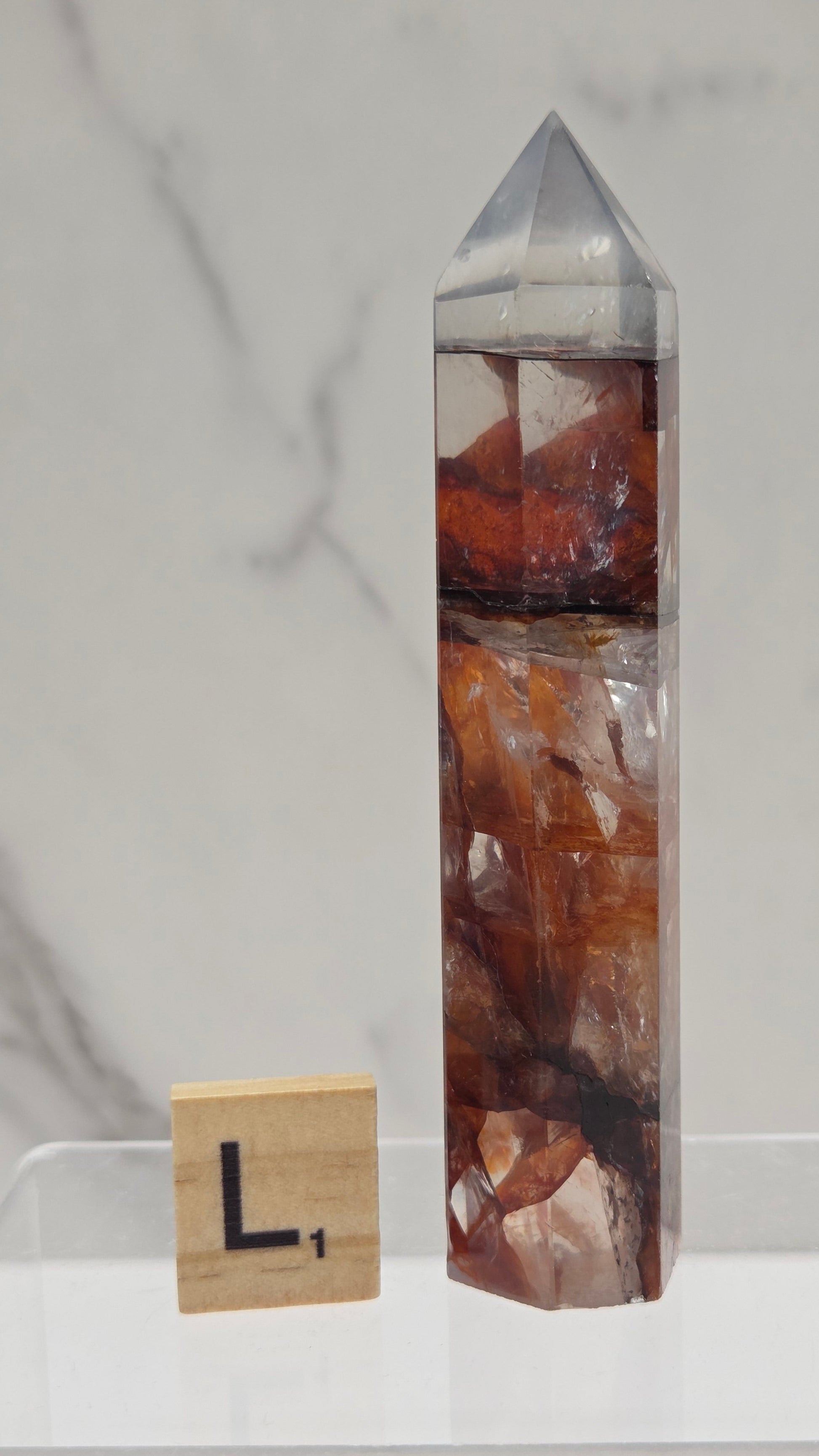 fire quartz crystal point on a white stand against a marble background