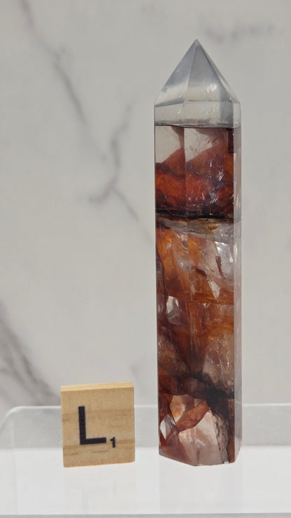 fire quartz crystal point on a white stand against a marble background