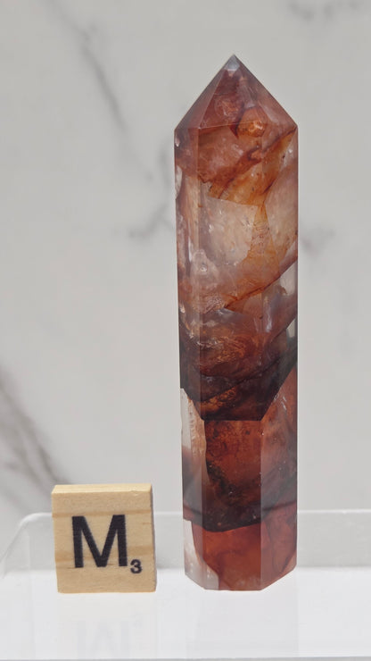 fire quartz crystal point on a white stand against a marble background