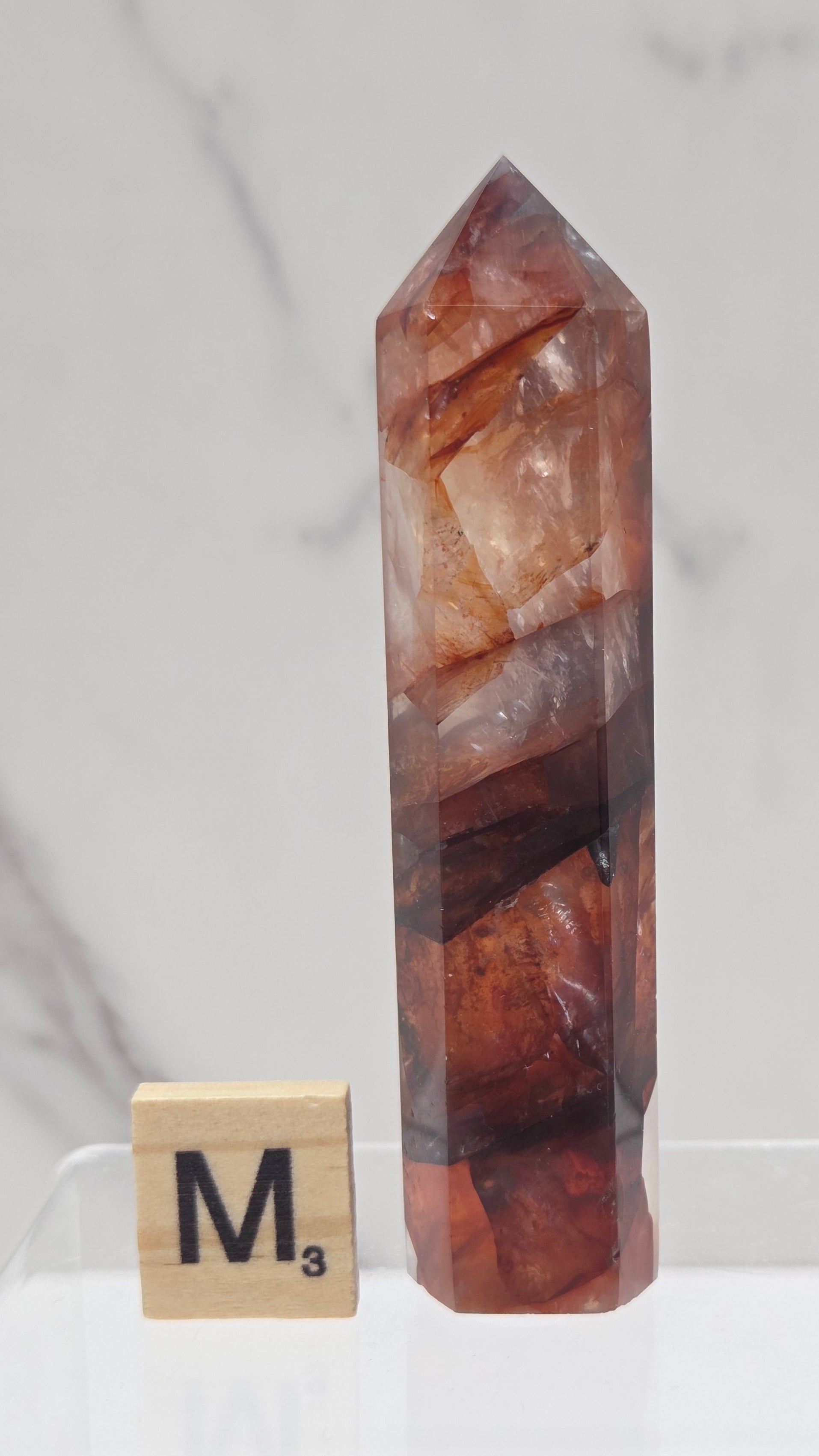 fire quartz crystal point on a white stand against a marble background