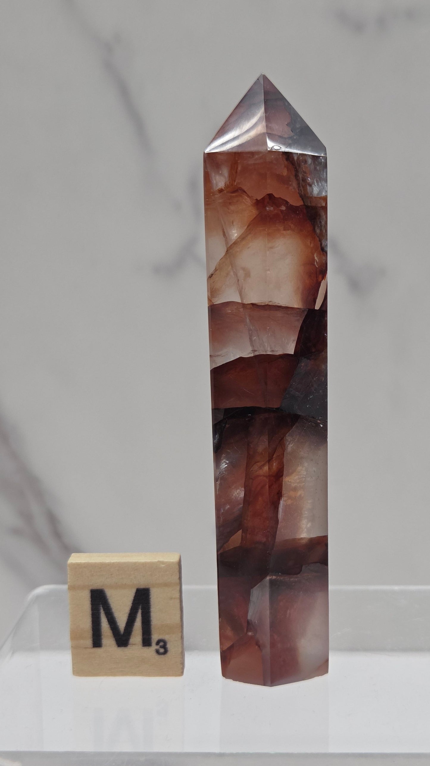 fire quartz crystal point on a white stand against a marble background