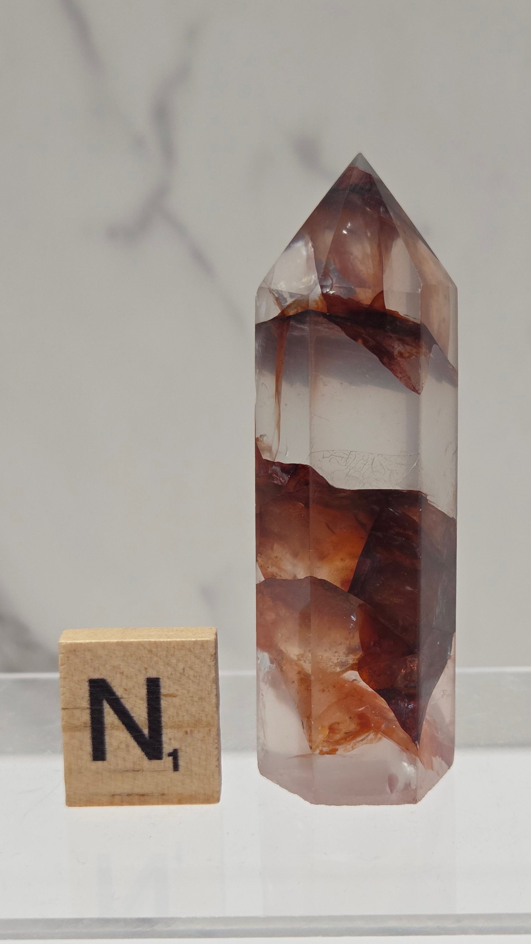 fire quartz crystal point on a white stand against a marble background