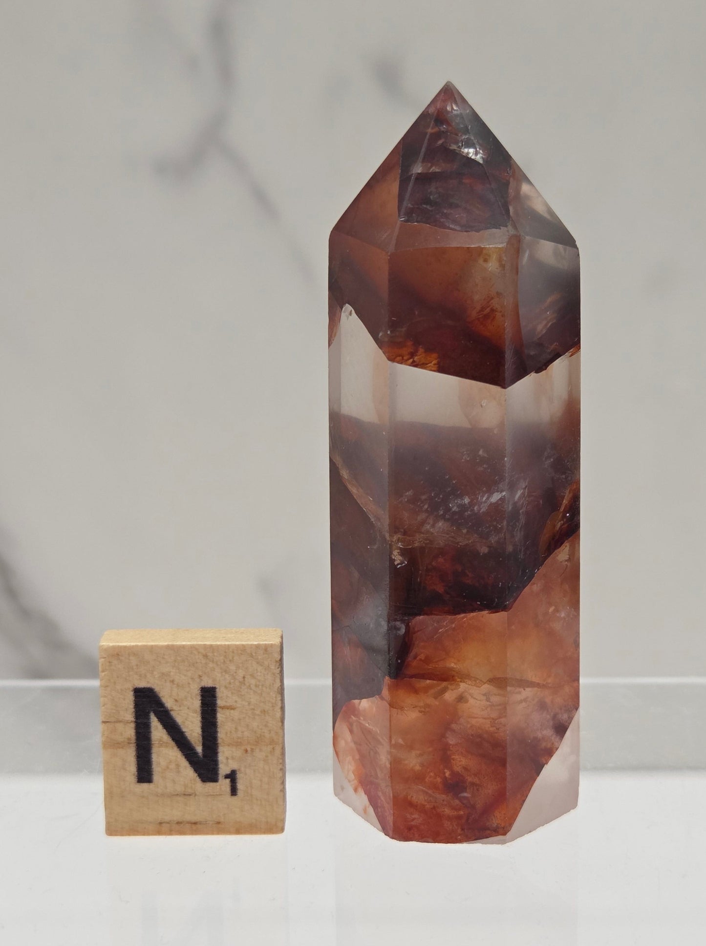 fire quartz crystal point on a white stand against a marble background