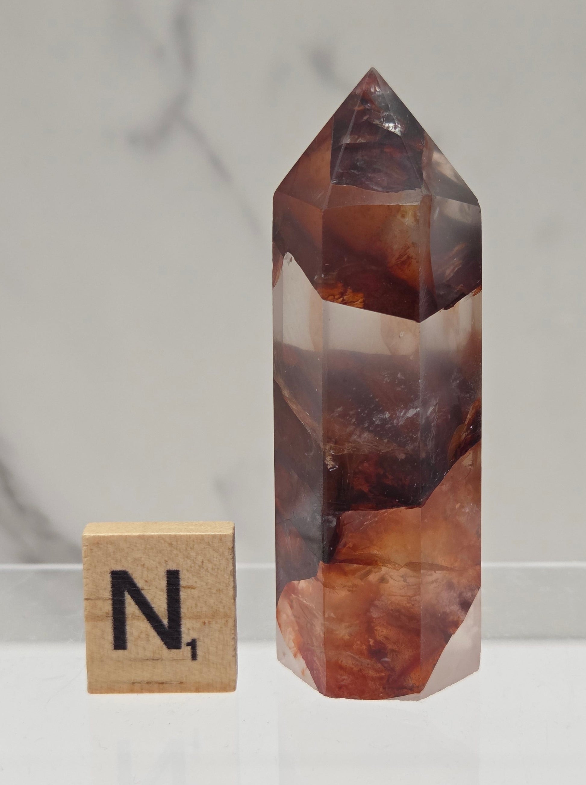 fire quartz crystal point on a white stand against a marble background
