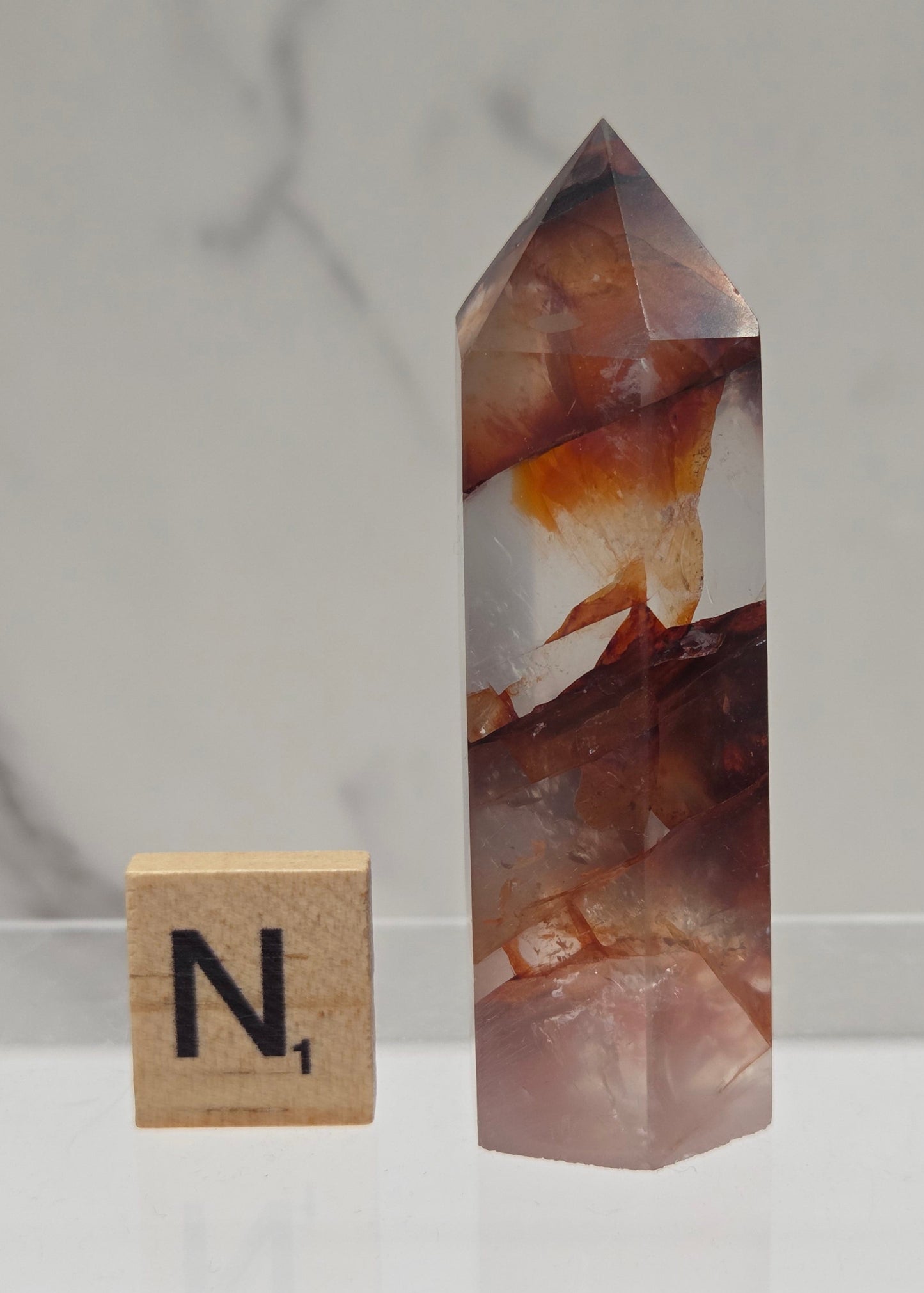 fire quartz crystal point on a white stand against a marble background