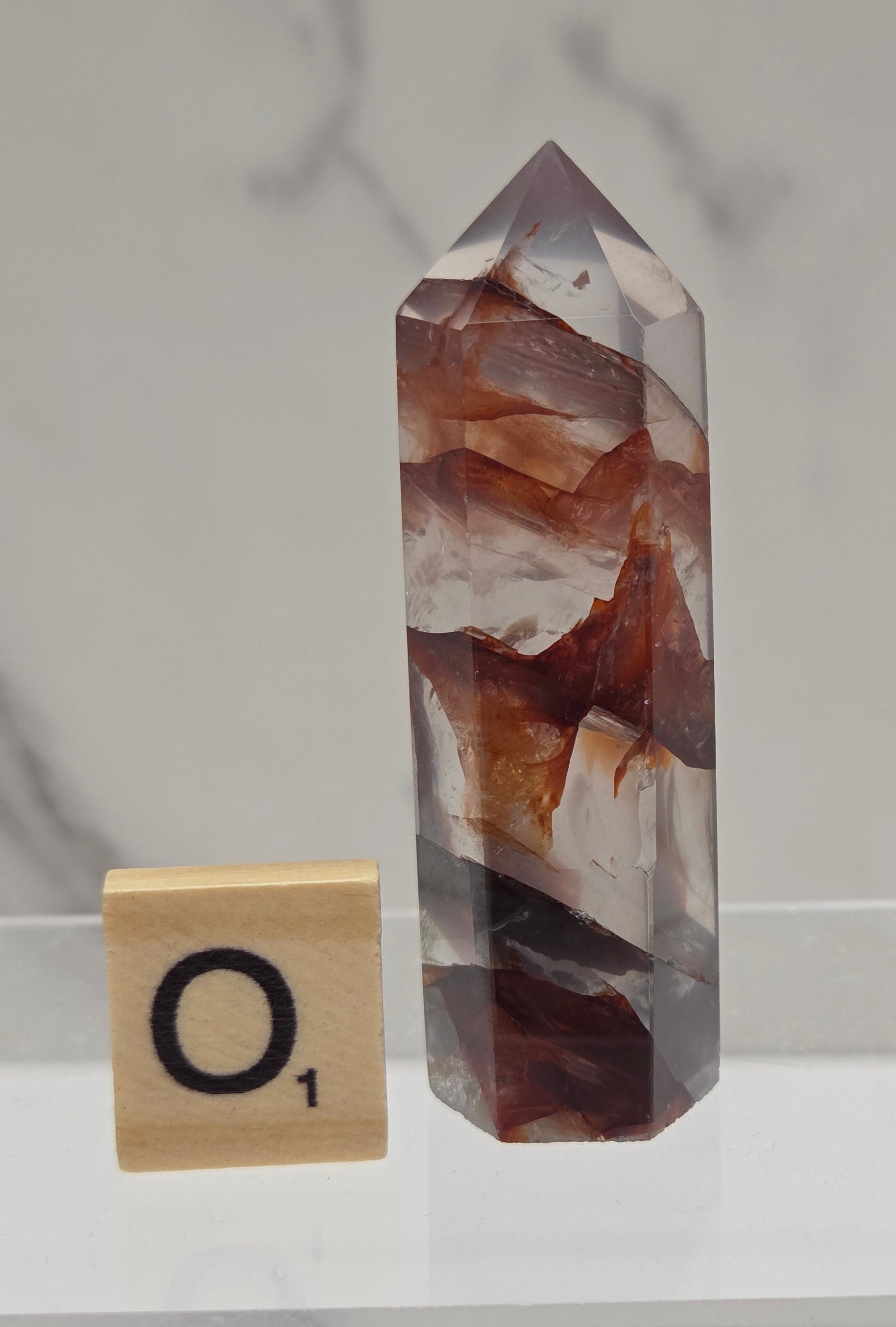 fire quartz crystal point on a white stand against a marble background