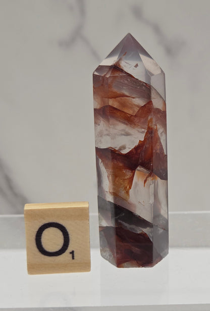 fire quartz crystal point on a white stand against a marble background