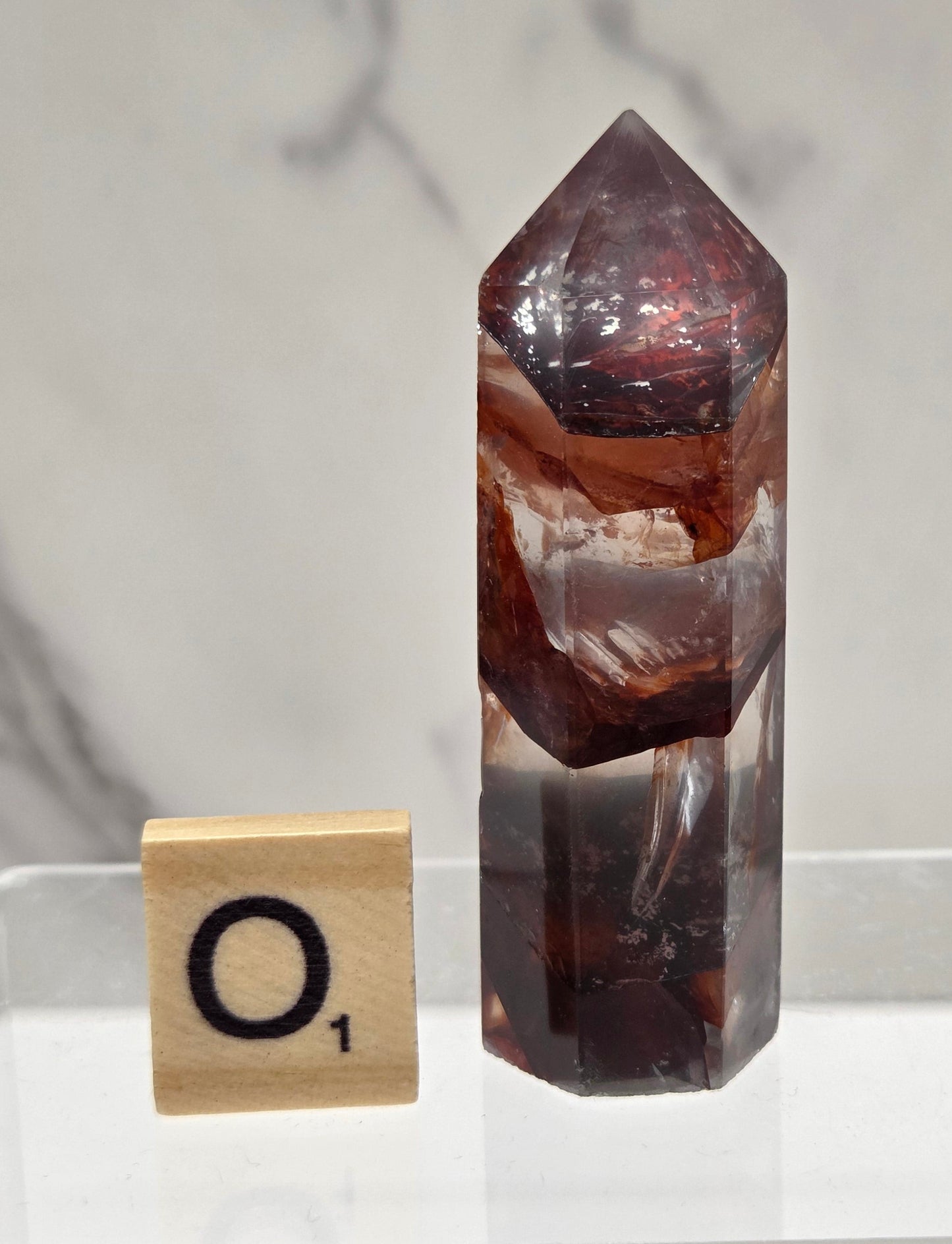 fire quartz crystal point on a white stand against a marble background