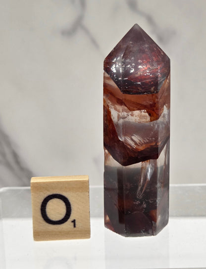 fire quartz crystal point on a white stand against a marble background