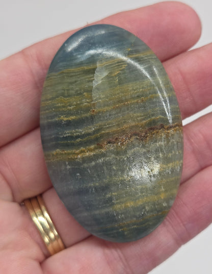 Hand holding a smooth, oval-shaped Blue Onyx palm stone with banded patterns of blue, white, and brown.