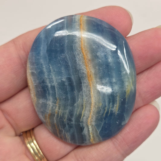 Blue Onyx cabochon with yellow veins held in a hand against a white background