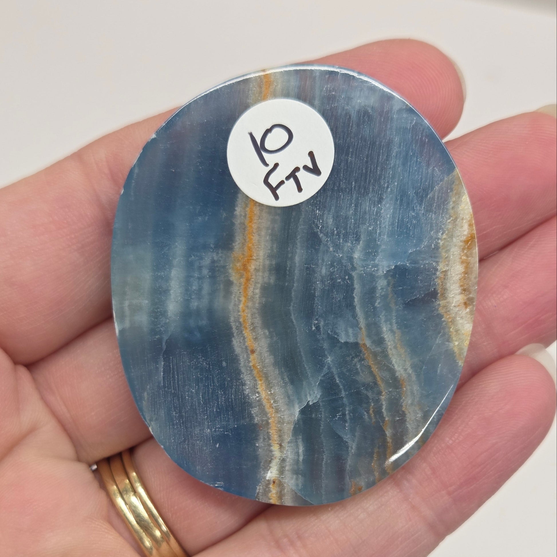 Blue Onyx cabochon with yellow veins held in a hand against a white background