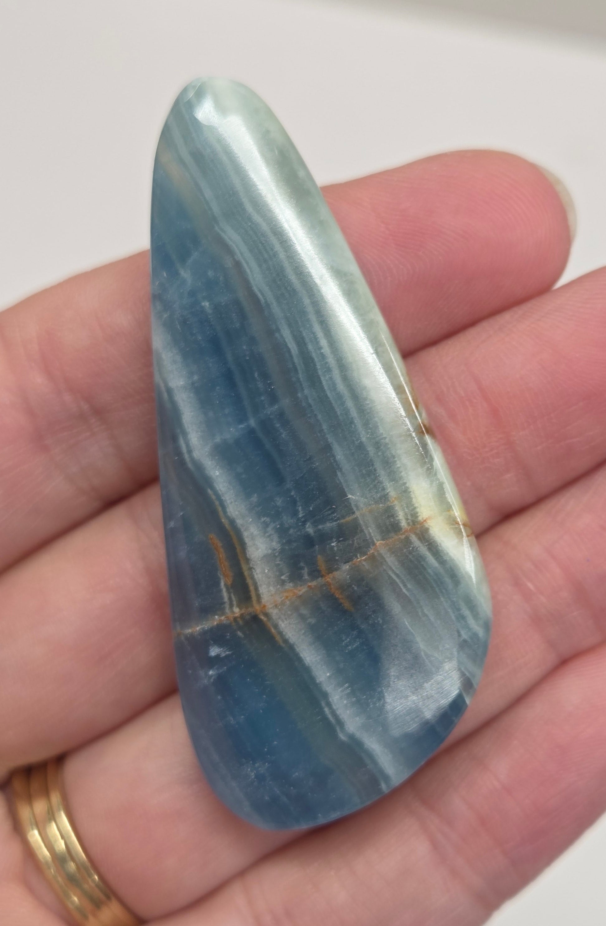 Blue Onyx cabochon with yellow veins held in a hand against a white background