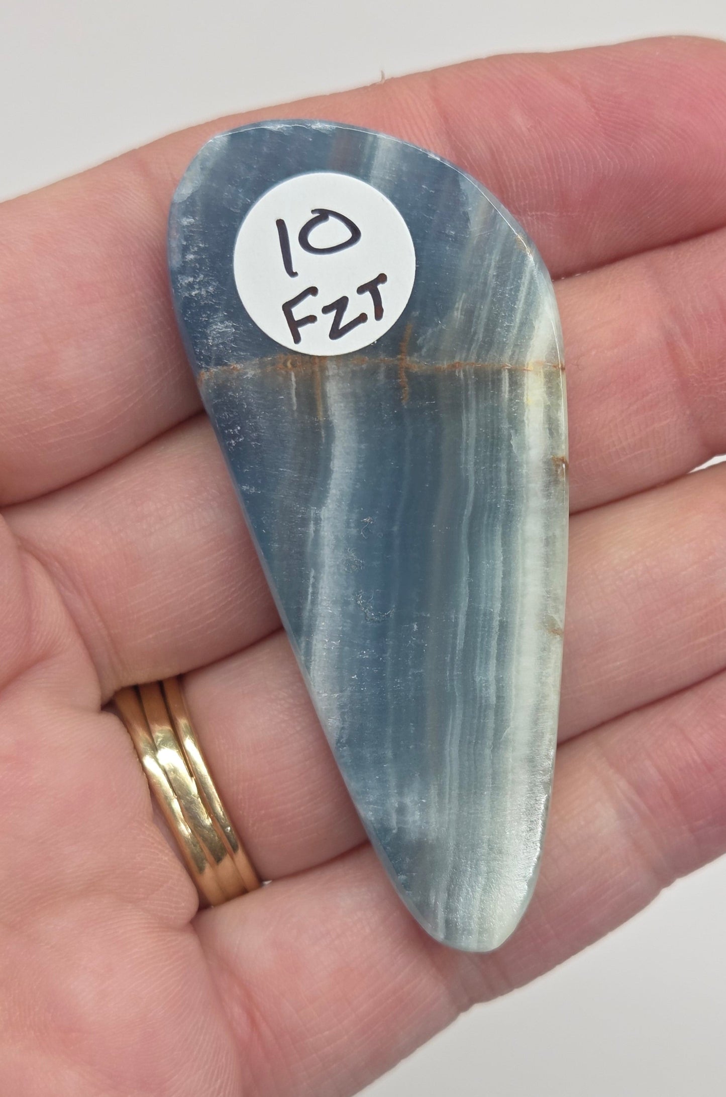 Blue Onyx cabochon with yellow veins held in a hand against a white background