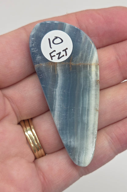Blue Onyx cabochon with yellow veins held in a hand against a white background