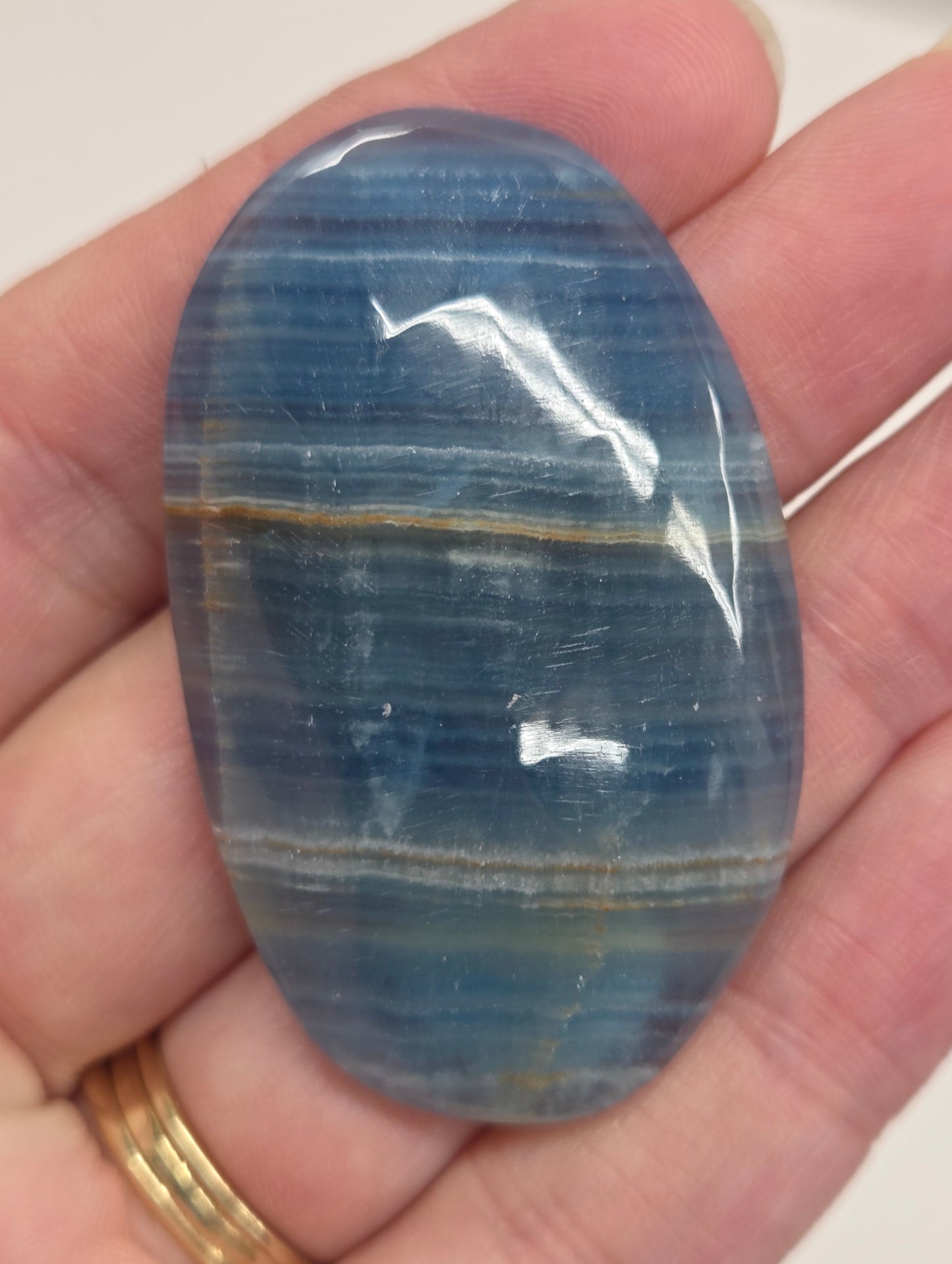 Blue Onyx cabochon with yellow veins held in a hand against a white background