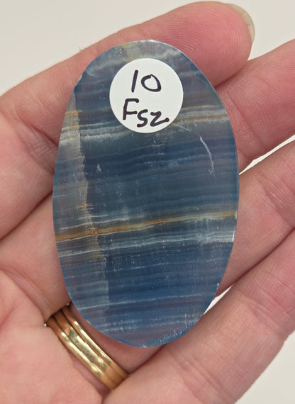 Blue Onyx cabochon with yellow veins held in a hand against a white background