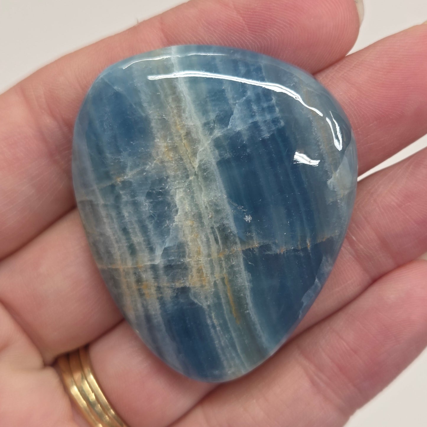 Blue Onyx cabochon with yellow veins held in a hand against a white background