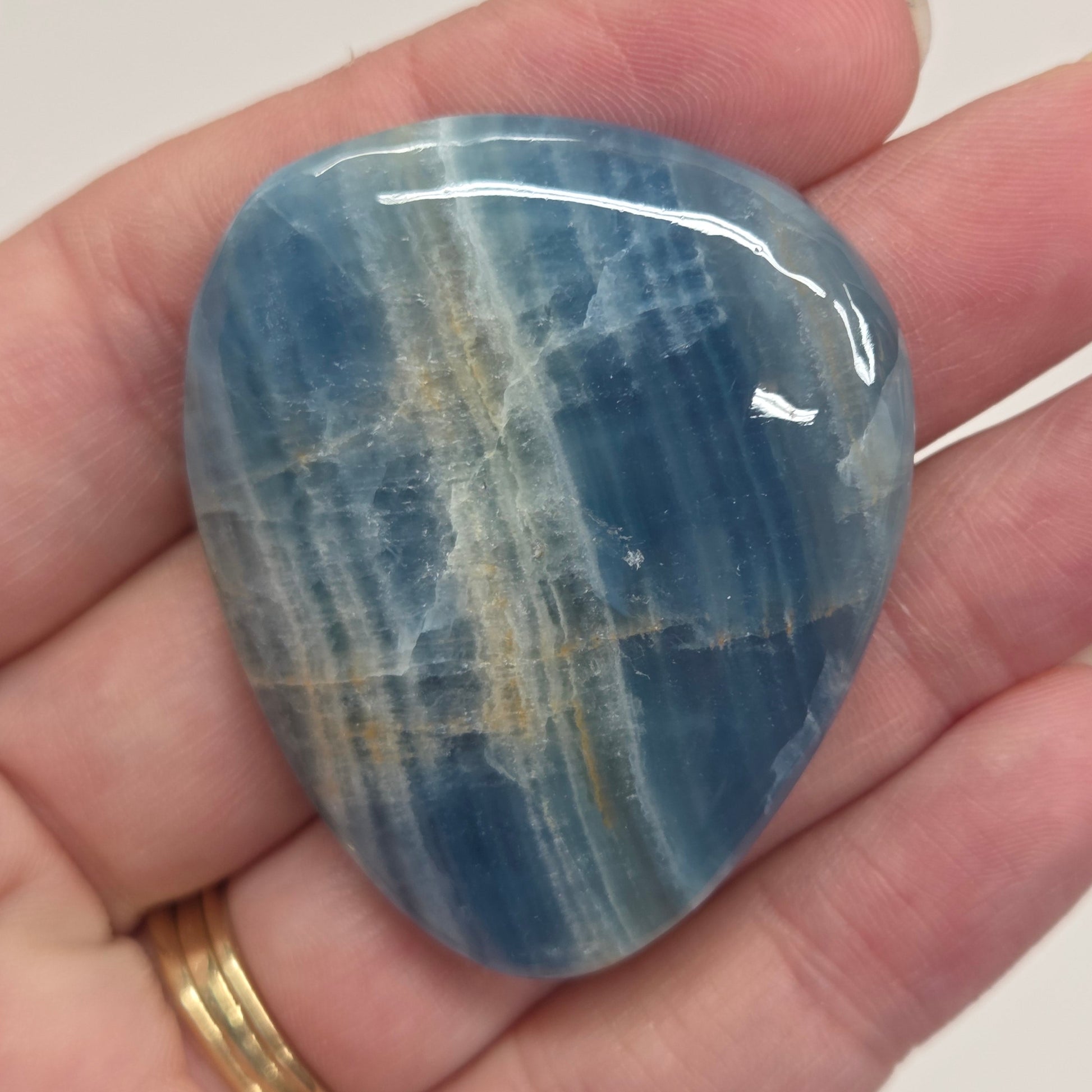Blue Onyx cabochon with yellow veins held in a hand against a white background