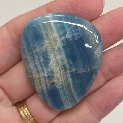 Blue Onyx cabochon with yellow veins held in a hand against a white background