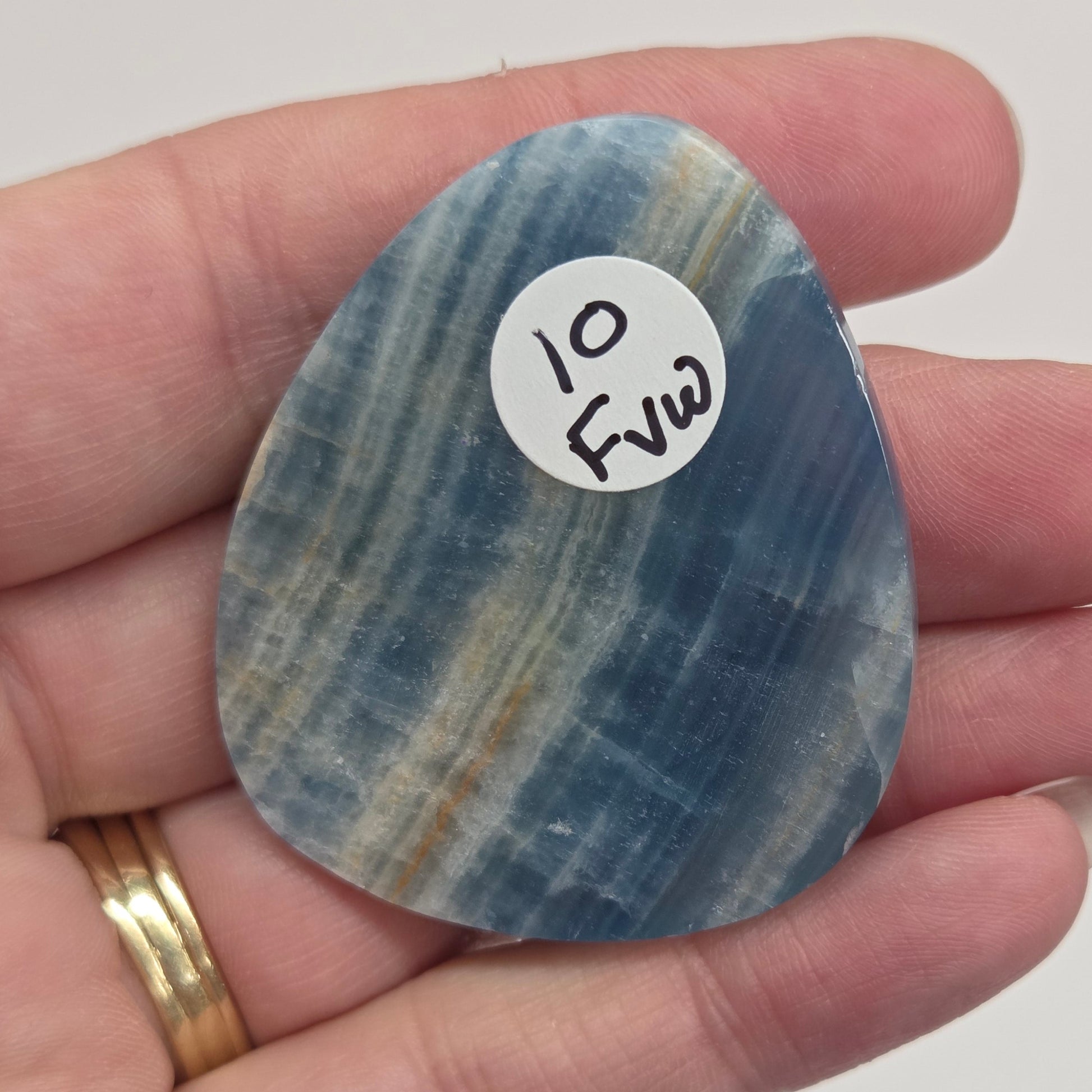 Blue Onyx cabochon with yellow veins held in a hand against a white background