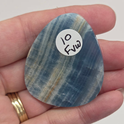 Blue Onyx cabochon with yellow veins held in a hand against a white background