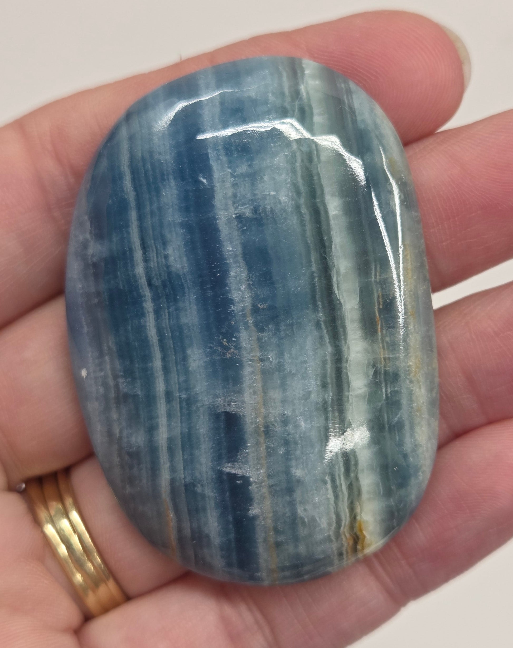 Blue Onyx cabochon with yellow veins held in a hand against a white background