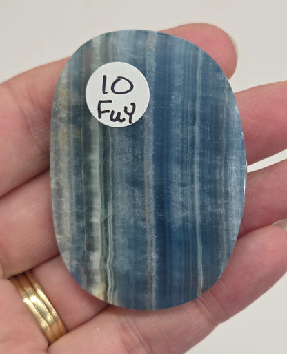 Blue Onyx cabochon with yellow veins held in a hand against a white background
