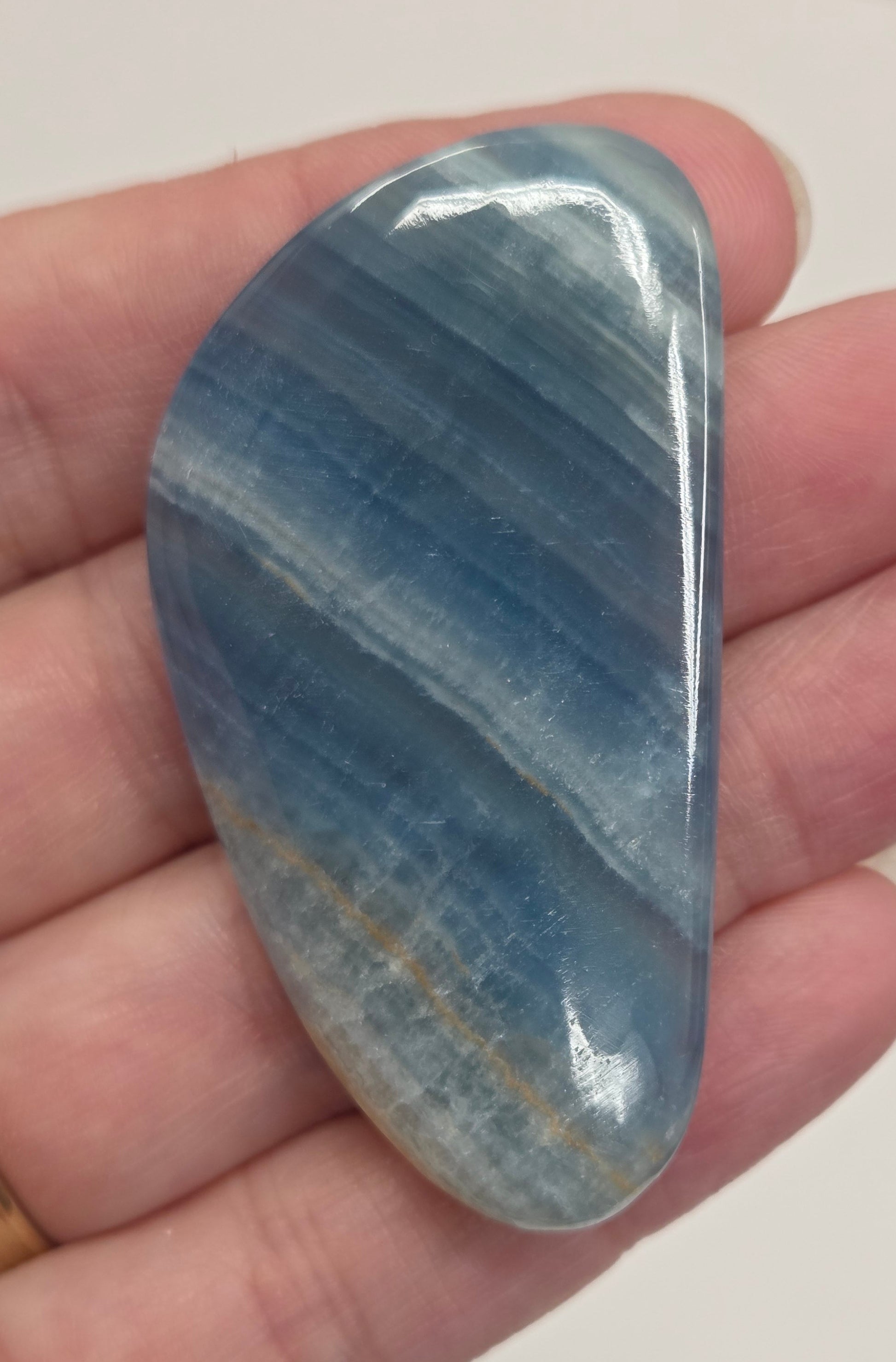 Blue Onyx cabochon with yellow veins held in a hand against a white background