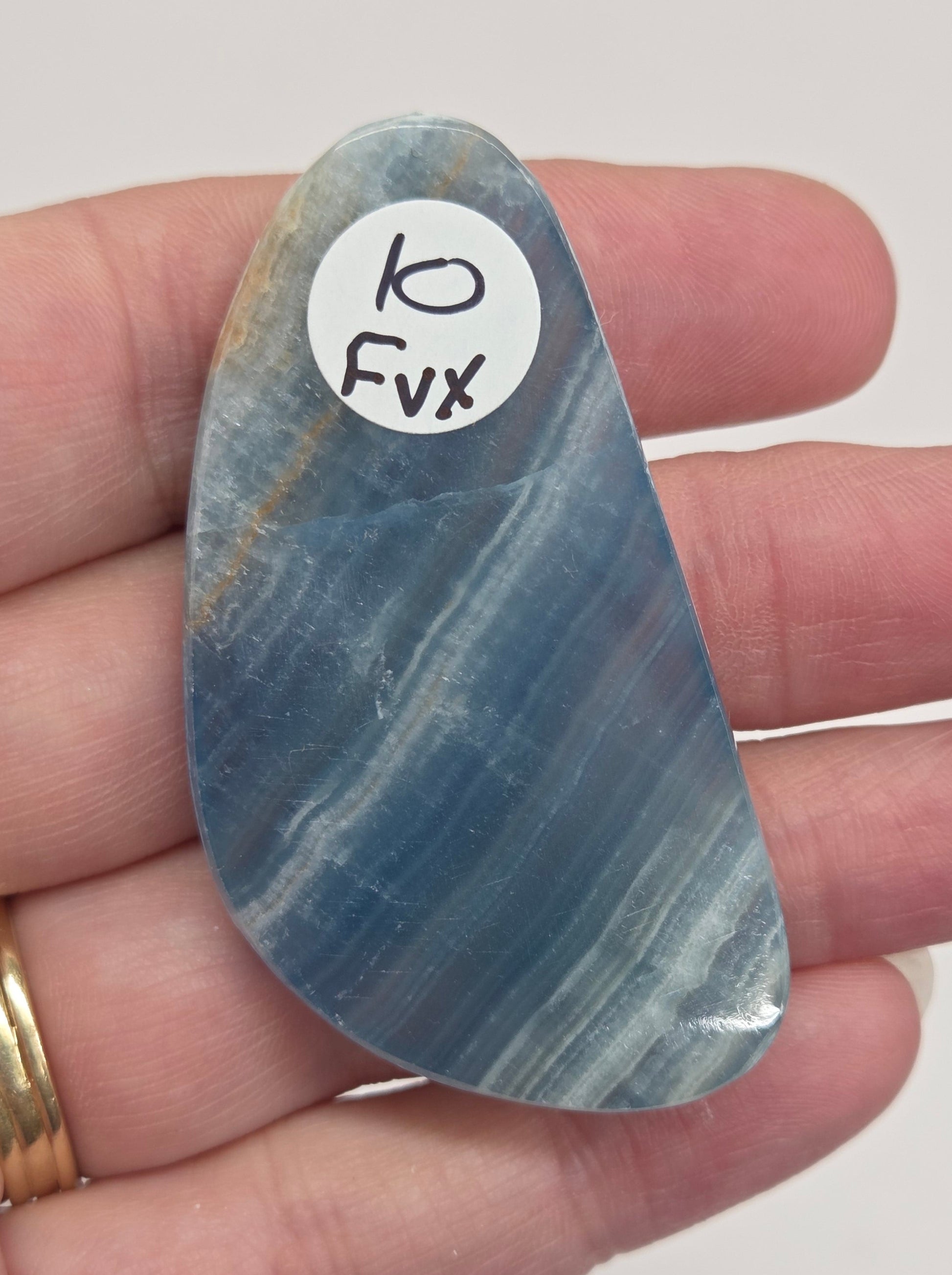 Blue Onyx cabochon with yellow veins held in a hand against a white background