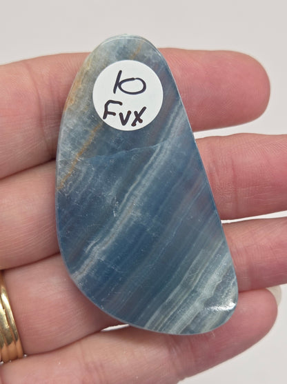 Blue Onyx cabochon with yellow veins held in a hand against a white background