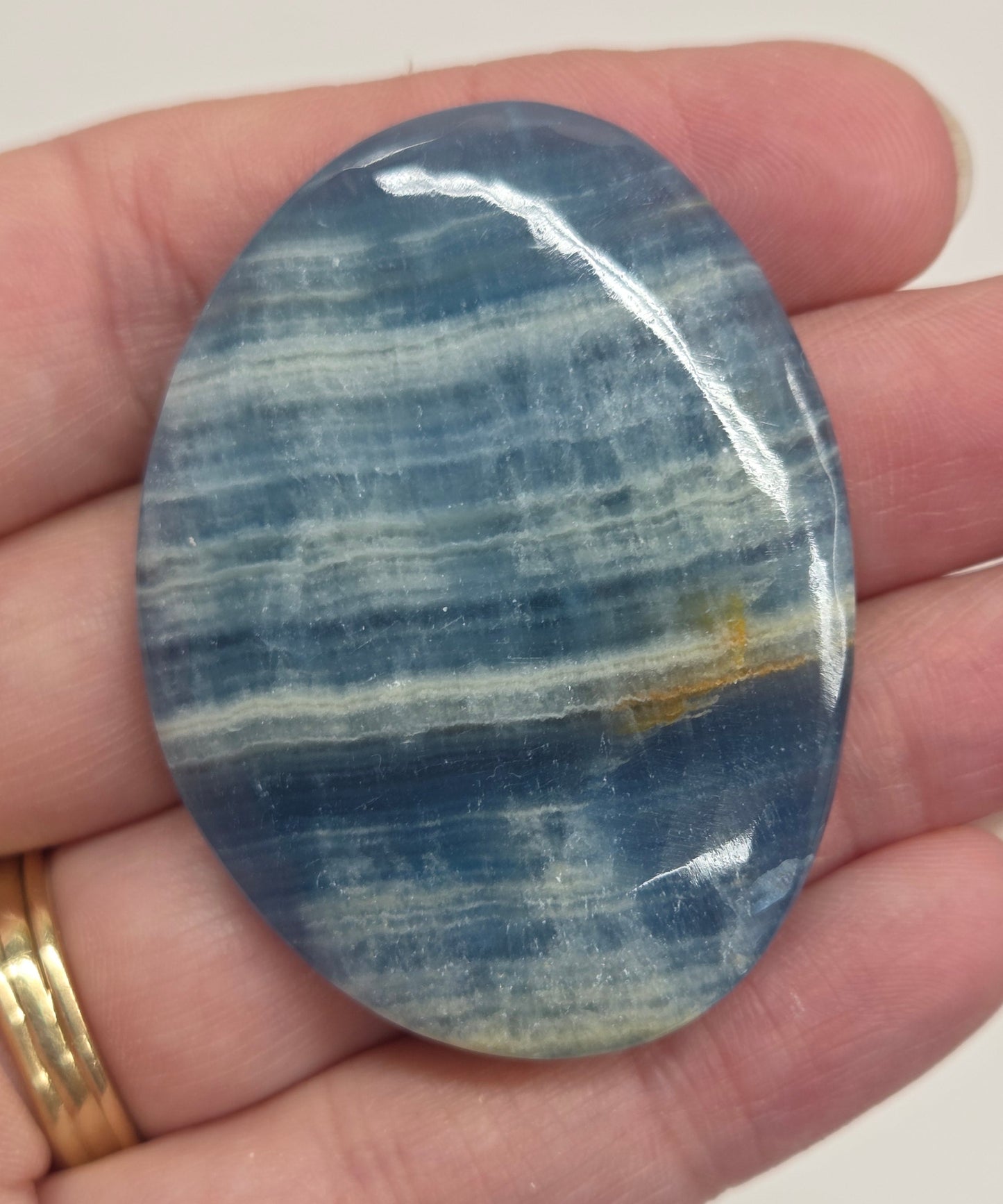Blue Onyx cabochon with yellow veins held in a hand against a white background
