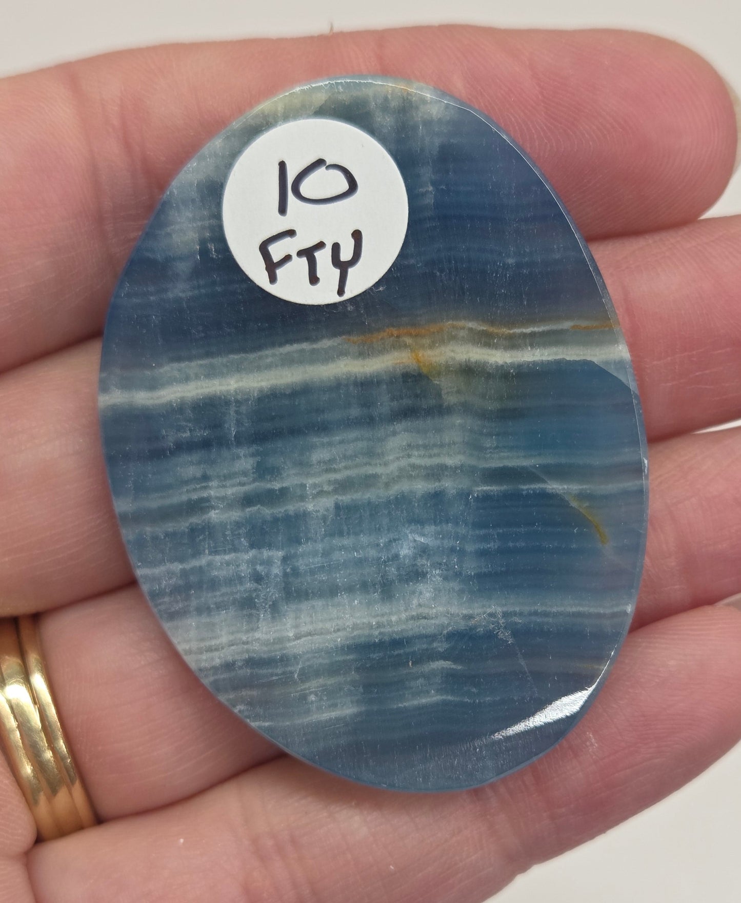 Blue Onyx cabochon with yellow veins held in a hand against a white background