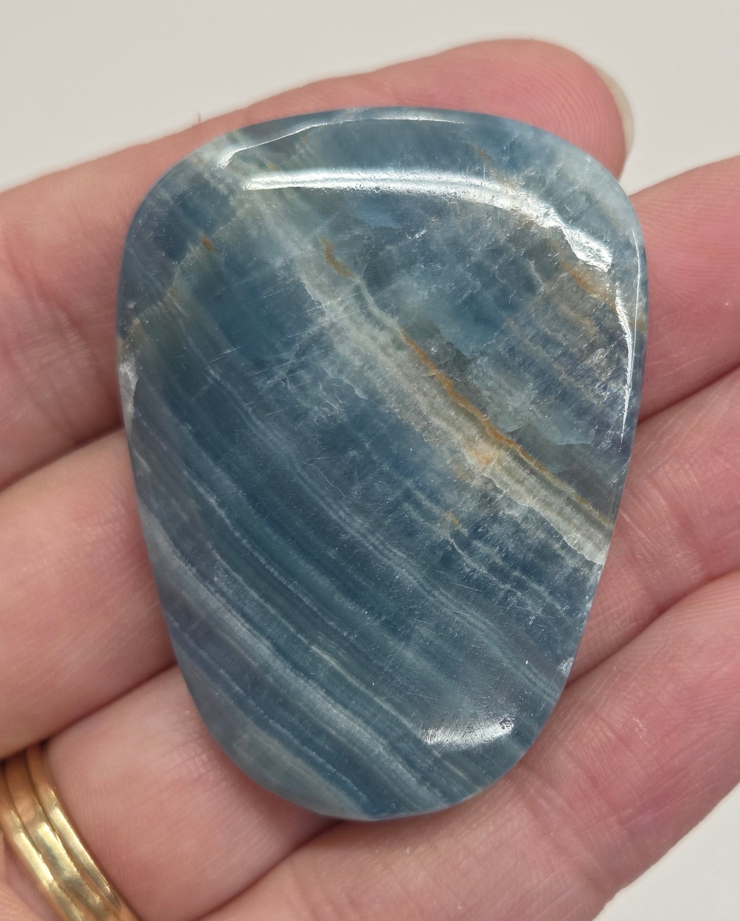 Blue Onyx cabochon with yellow veins held in a hand against a white background