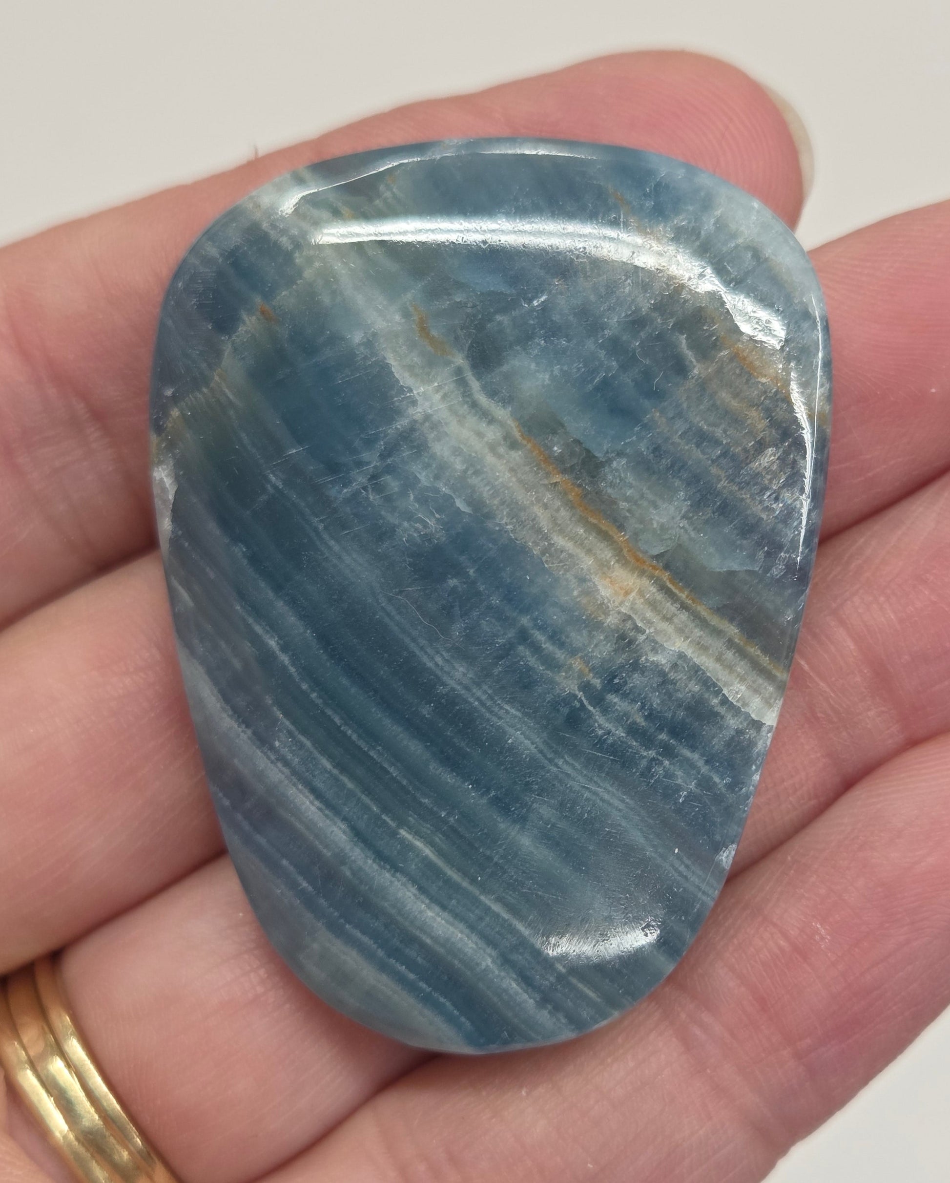 Blue Onyx cabochon with yellow veins held in a hand against a white background