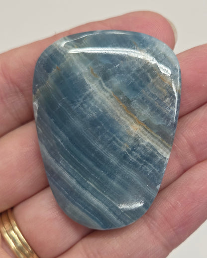 Blue Onyx cabochon with yellow veins held in a hand against a white background